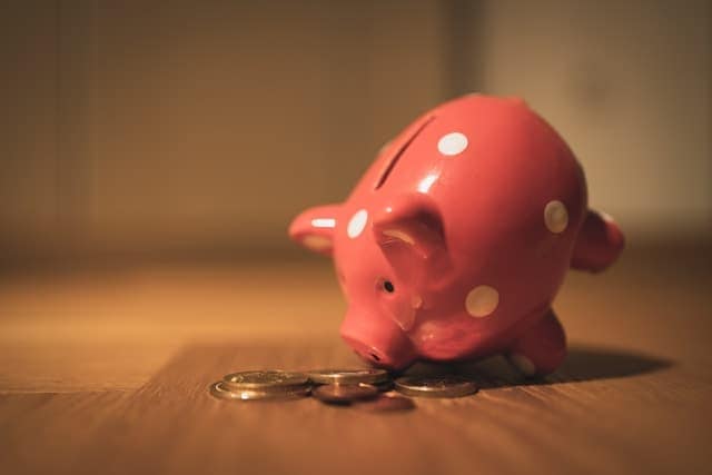A pink ceramic piggy bank with white polkadots, leaning forward to sniff coins