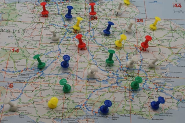 A printed map of South East England, multiple, colourful pins embedded into it.